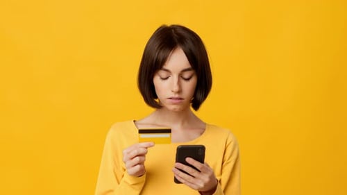 Young Brunette Woman Engages in Online Shopping with Phone and Credit Card