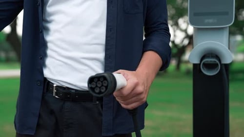 Man recharging battery for electric car during road trip. Exalt