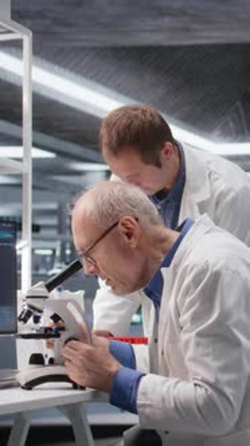 Laboratório de Vídeo Vertical com Velho Cientista Masculino Observando Espécime Sob Microscópio