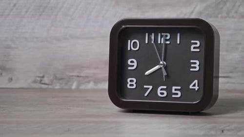 Die Zeigeruhr in quadratischer Form auf dem Holztisch zeigt die Uhrzeit 8 Stunden an