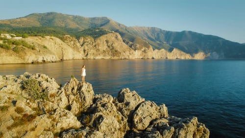 Woman on rocky cliffs overlooking calm blue sea at sunset in Kefalonia Greece