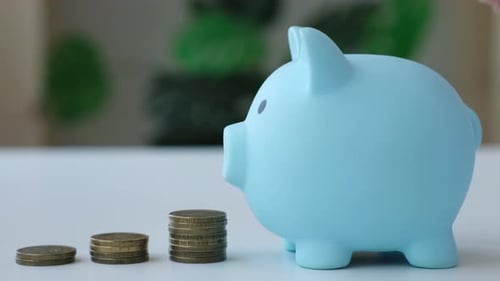 Hand Putting Coins in Blue Piggy Bank Close Up Savings Investing in Future