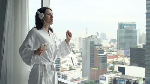 Woman in Bathrobe Listening to Music in City Apartment