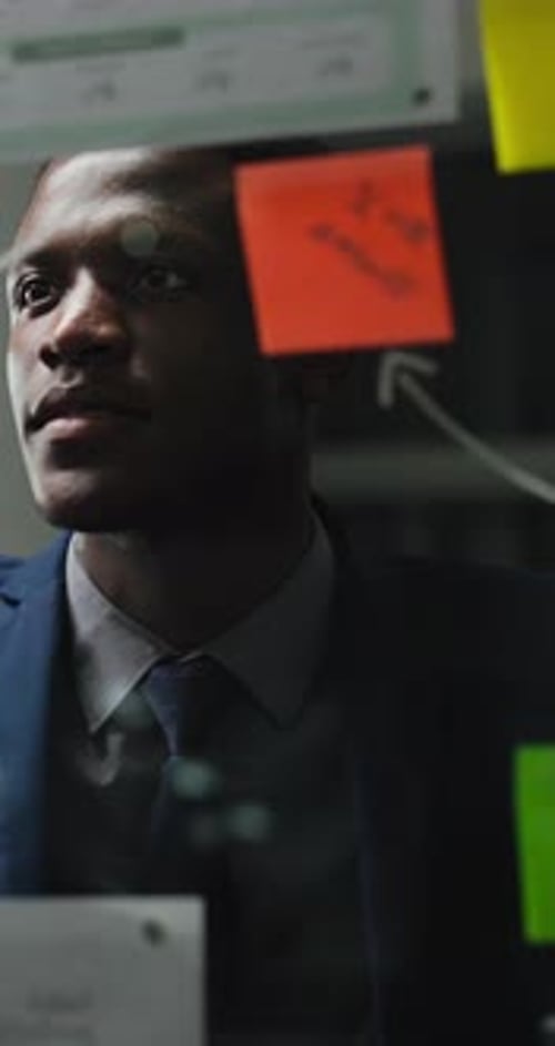 Focused Man Reviews Sticky Notes on Glass Board