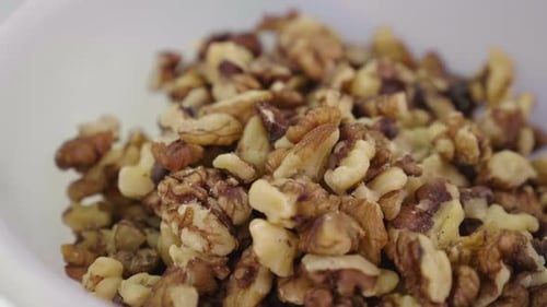 A white ceramic bowl full of peeled walnuts in close up. Daylight. Cooking ingredient. Nut snack.