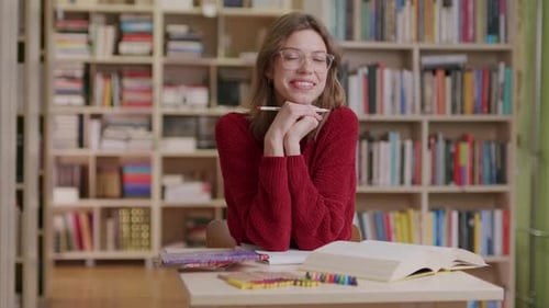 A young beautiful female student smiles into the camera while studying in the library—medium shot.