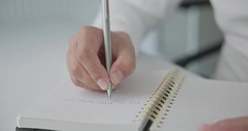 Closeup of Hands a Man in a Shirt Writes with a Pen and Takes Notes in a Notepad on a Metal Spring