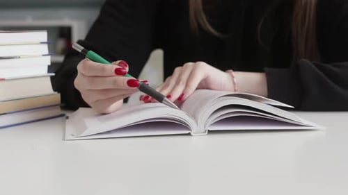 Woman with Red Manicure Underlining Text in Book with Green Pencil Closeup