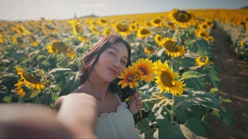 Young smiling asian woman taking selfie photo and video with mobile smartphone in sunflower field