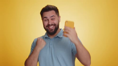 Excited Man Using Smartphone on Yellow Background