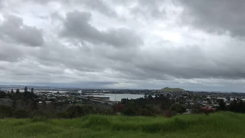 Zeitraffer grauer Wolken, die sich schnell über einem grasbewachsenen Vordergrund bewegen, mit dem Stadtbild im Hintergrund