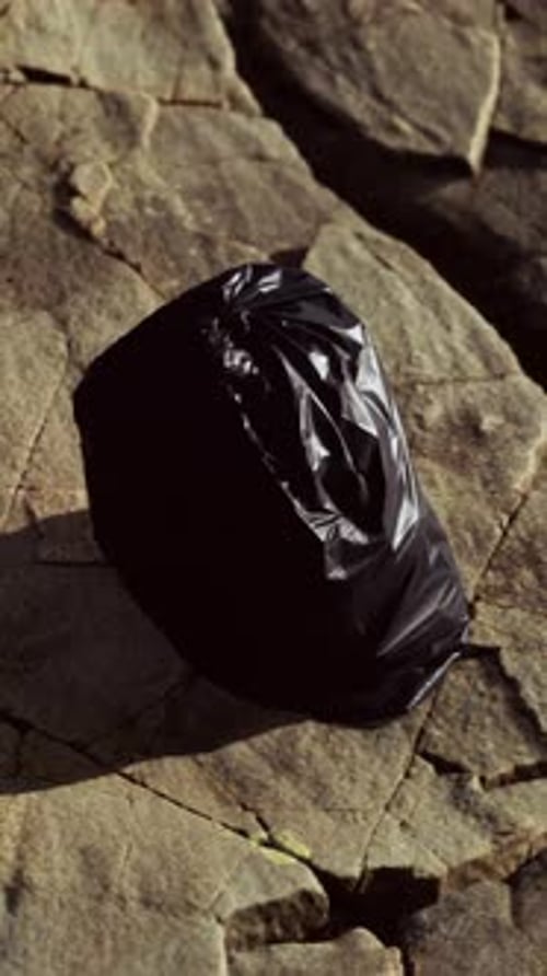 Black Trash Bag Lay on a Rocky Beach