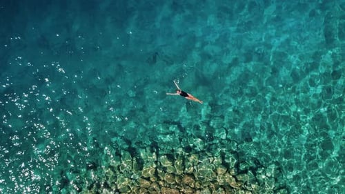 Single Tourist Floating on the Surface of the Serene Sea. Rocky seabed and the calm water surface. P