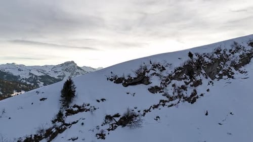 Aerial revealing flight over slope of mountains showing snowy mountain range during sunset time in A
