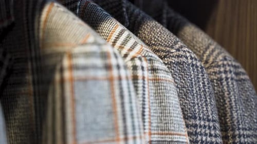 Patterned tailored tweed jackets hanging in wooden wardrobe, close up.
