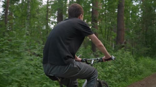 Young Boy Riding Bicycle Along Forest Path with Blurred Cyclist in Distance