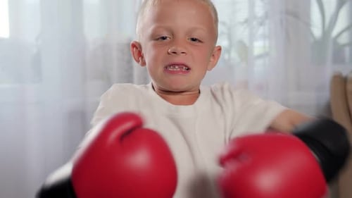 Nahaufnahme eines kleinen Jungen in Boxhandschuhen, der zu Hause Schläge übt