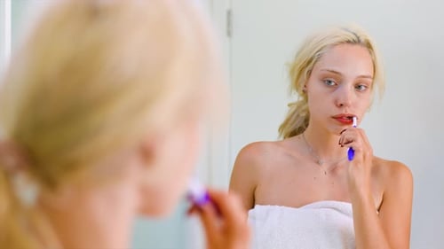 Woman Brushing Teeth in Bathroom Mirror