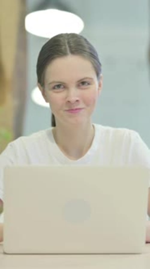 Smiling Woman in White Shirt Sits at Computer