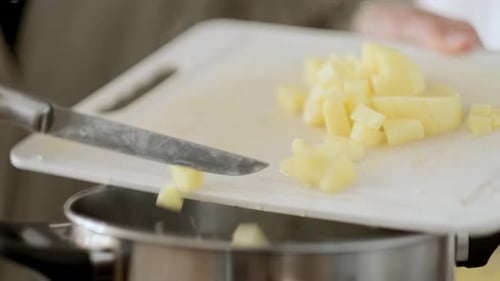 Mãos de mulher colocando batatas picadas da tábua de cortar em uma panela de água fervente ou caldo para cozinhar