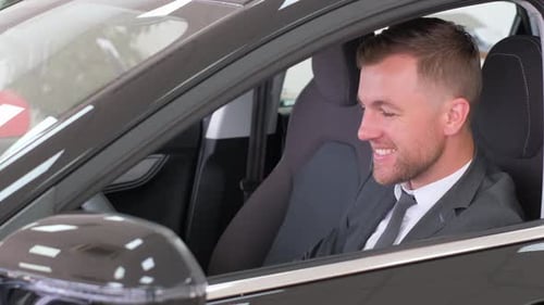 Man Sits in New Car at Auto Dealership