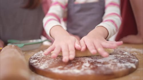 A family helping their daughter roll dough together in the kitchen, enjoying a fun baking moment
