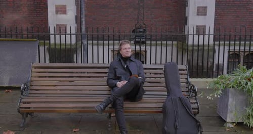 Un musicien contemplatif est assis paisiblement sur un banc de parc en profitant de la nature sereine