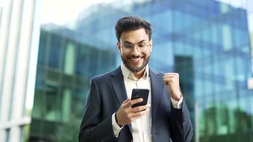 Excited Man Checks Phone Outside Modern Building