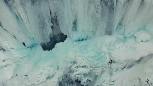 Aerial close up shot of top view of frozen crystal iced waterfall icicles in snowy mountains in wi