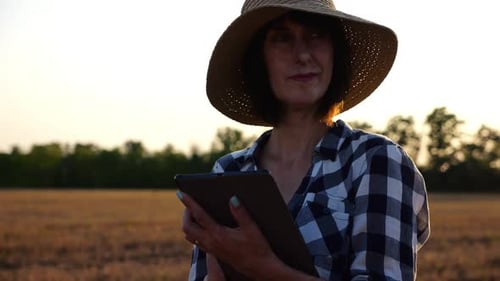Female Agronomist in Straw Hat Monitoring Harvest on Barley Field at Sunset Adult Farmer Using