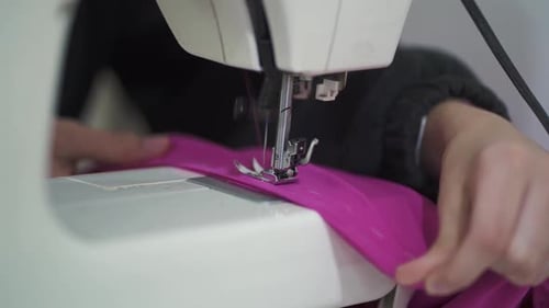 Close-up of hands using sewing on pink fabric at tailoring workshop