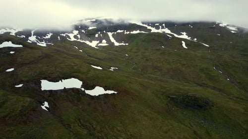 Snow Patches on Green Mountain Under Low Clouds – Norway Aerial