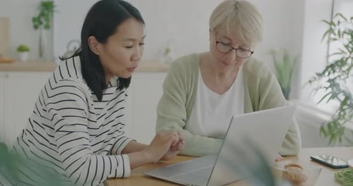 Female Volunteer Helping Senior Woman with Laptop Teaching Technology Talking and Using Computer at