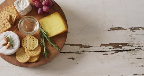 Vidéo de fromage, de biscuits, de raisins et de romarin sur une planche de bois et un plateau rustique avec espace de copie
