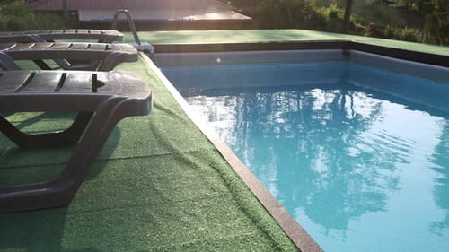 Empty sun loungers on artificial grass near outdoor swimming pool with inflatable ring