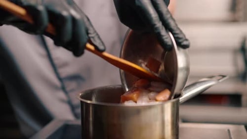 professional restaurant kitchen chef adding seafood to broth to prepare spicy soup tom yum asian