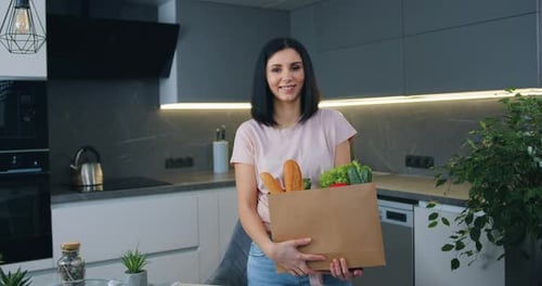 Happy woman with big food package and looking at camera while standing in modern kitchen