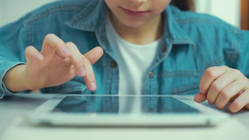 closeup of little girl in jeans wear playing games on tablet