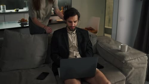 Un homme brun confiant avec du chaume dans une veste noire et un short beige travaille à distance avec un gris