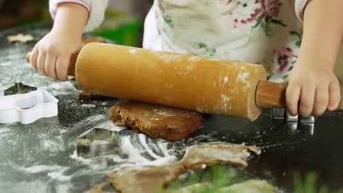Child rolling dough with wooden rolling pin for christmas cookies at home