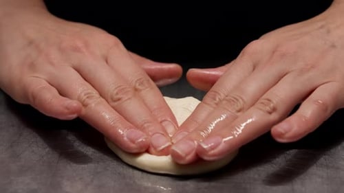 Hands Flattening Dough on Metal Table for Food Preparation