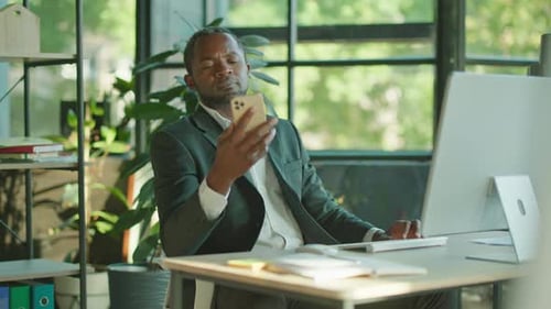 Footage of Confident Busy Middleaged African Man Working on Computer in Office Using Smartphone