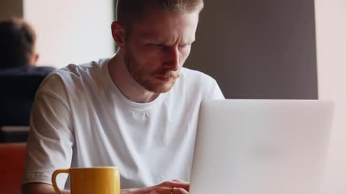 Un hombre serio está escribiendo en el teclado de su computadora portátil mientras está sentado en un café Un hombre trabaja de forma remota
