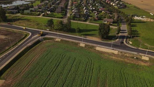 Aerial shot of a long, straight road cutting through vibrant green and golden fields on one side and
