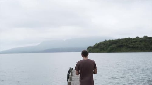 Man Piloting a Drone From a Wooden Bridge By the Sea at New Chums Beach New Zealand
