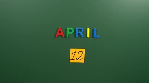 Hand sticking a sticker 12 April calendar day on school board. 12 date of April. Twelfth day