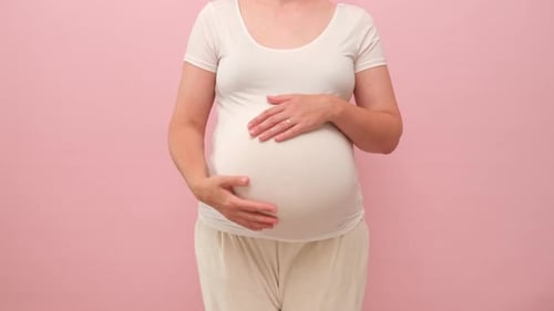 Pregnant woman holding her belly with two hands, studio pink background
