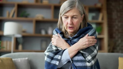 Femme senior aux cheveux gris recouverte d'une couverture gelée assise sur le canapé dans le salon à la maison. Bouleversé