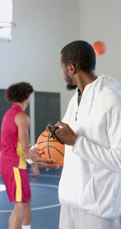 Vertical video: Holding basketball, coach observing player practicing ...