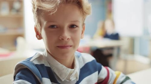 Portrait of a Cute Little Boy with Wavy Blond Hair Sitting at his School Desk, Smiles Happily. Smar